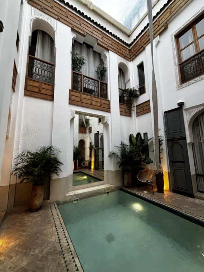 The inner courtyard with pool at a riad in Marrakech. White walls, tiles, plants, balconies. The pool is reflected in a large mirror