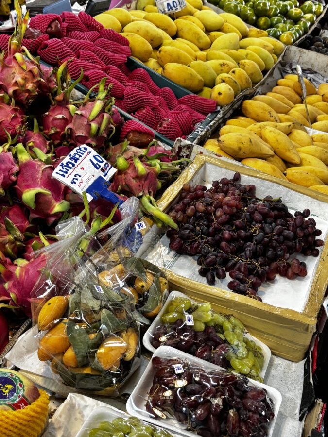 A close up of a market stand with mangos, grapes, dates and other tropical fruit, market in Thailand