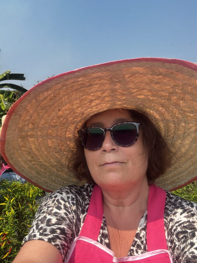 Woman with large straw hat, sunglasses and pink apron, doing a Thai cooking class in Chiang Mai