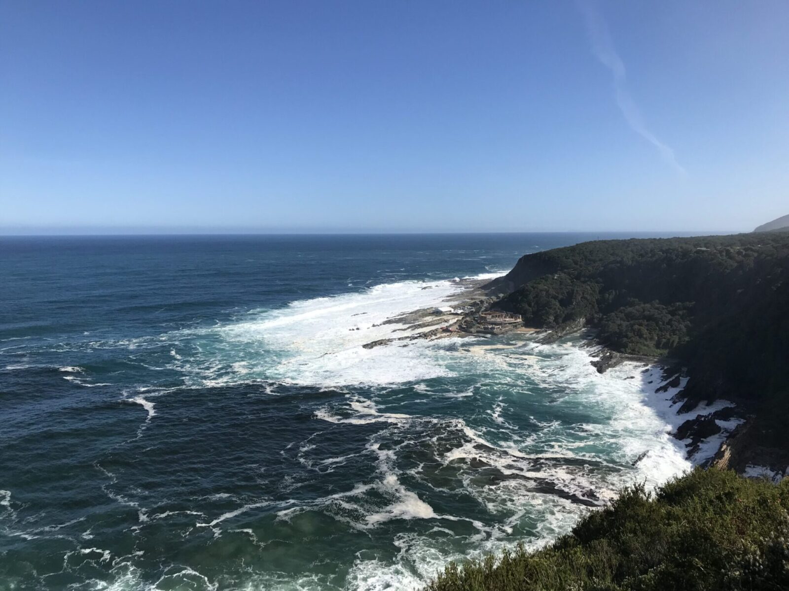 View of ocean and coast with high crashing waves against a bright blue sky