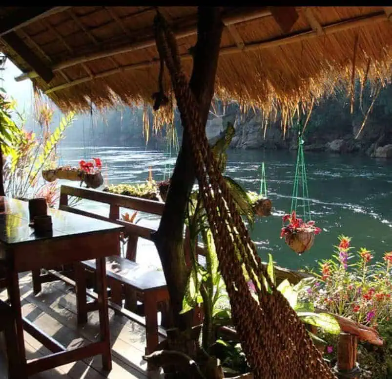 View from the hut at River Kwai Jungle Rafts: hammock, plants and the river floating by behind some hanging plants.