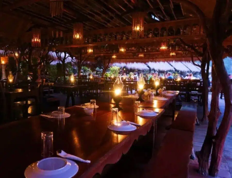 Plates and glasses on a wooden table with lit oil lamps, at dusk