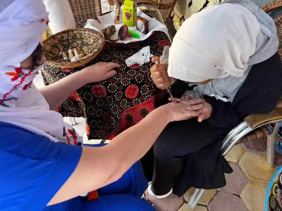 Alt text: Indigenous woman getting a tattoo on her hand by another woman, traditional design seen.