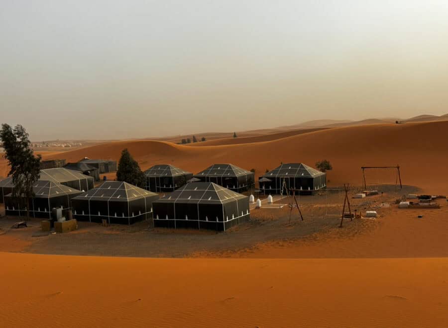 Campsite in the desert with black tents amidst shifting sand dunes and scenic landscape.