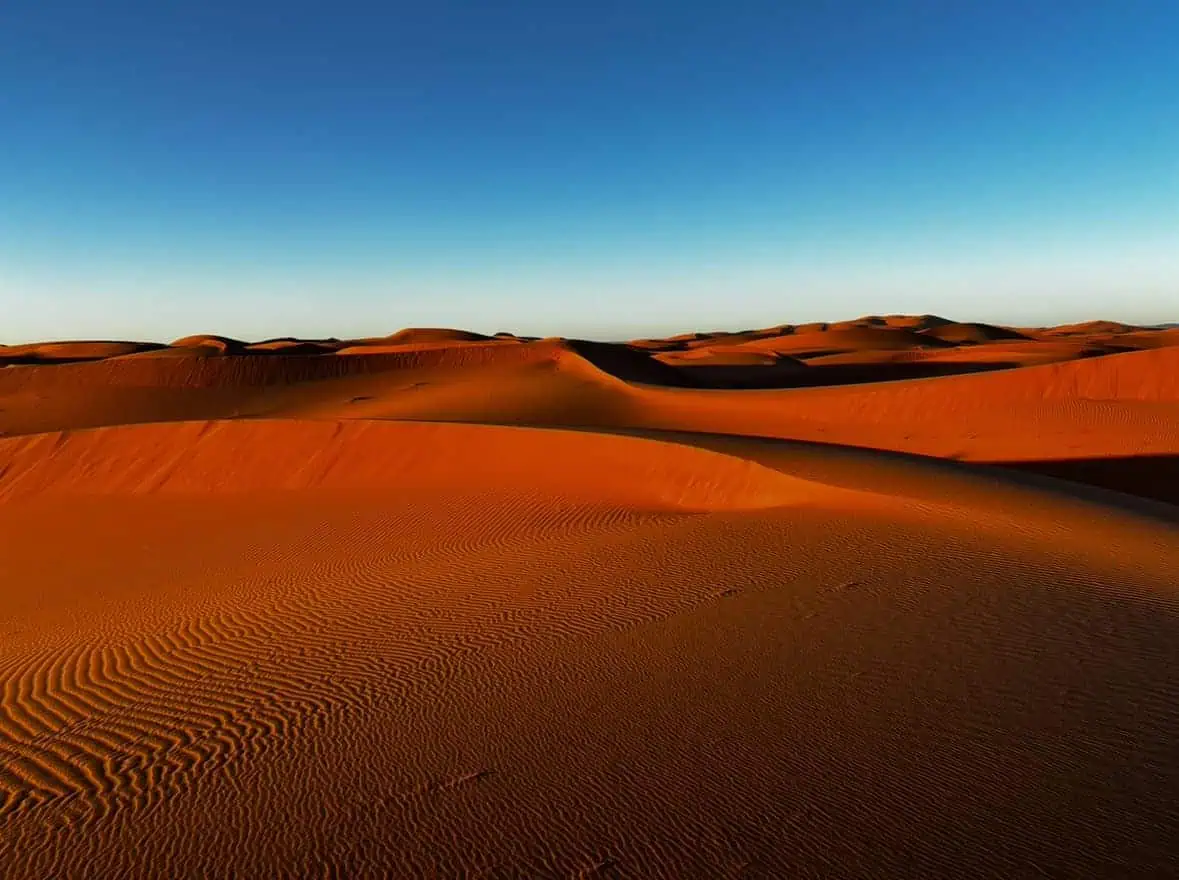 Vast desert dunes with red sands, flowing off into the distance with bright blue sky, taken at sunrise in the Erg Chebbi Desert, Morocco