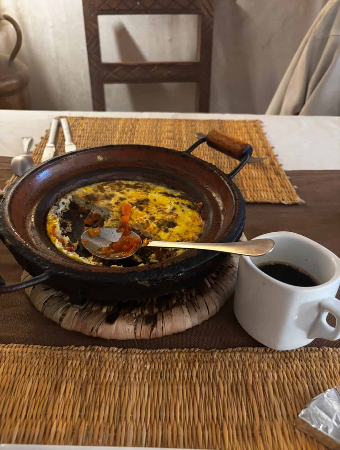 Rustic skillet breakfast with eggs, vegetables, and coffee on a woven placemat.