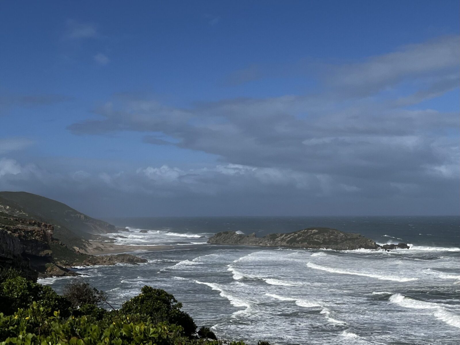 Dark clouds gathering over a see with high waves and part of the coastline in Robberg Nature Reserve. One of our best hikes on the Garden Route