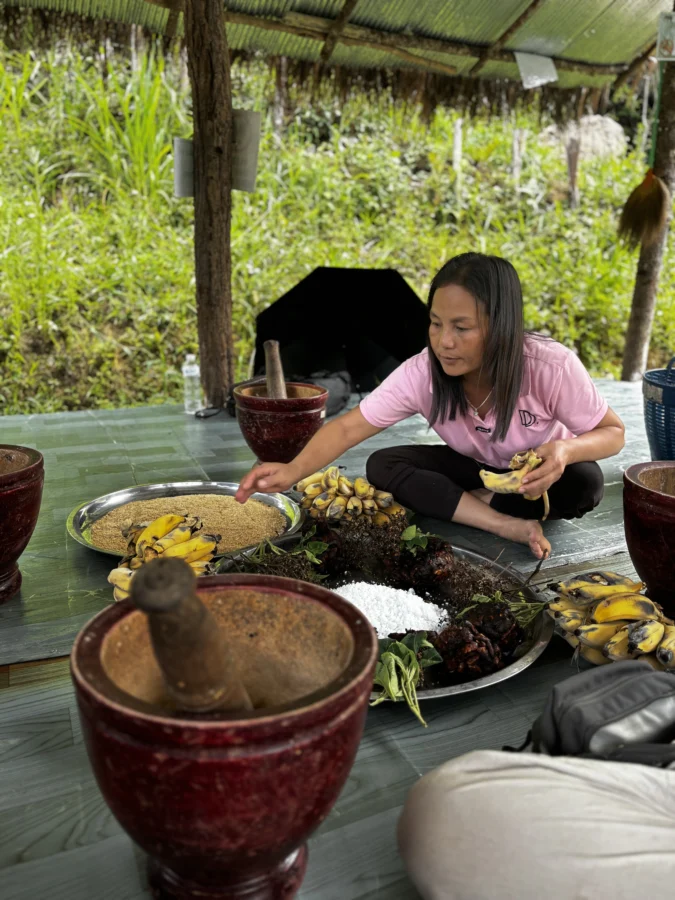 Woman in pink t-shirt sitting on the floor in an outdoor setting, surrounded by plates of food. 