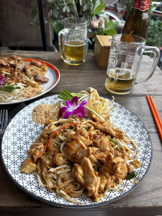 Plate of Pad Thai on a table, with two glasses of beer. 