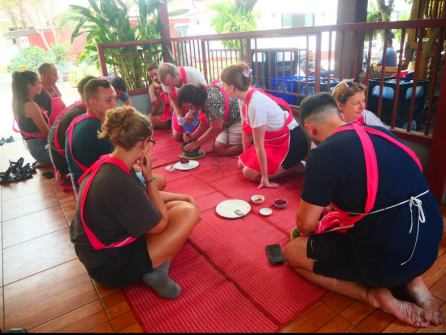 Making curry in Thai cooking class: woman using a mortar and pestle with group looking on.