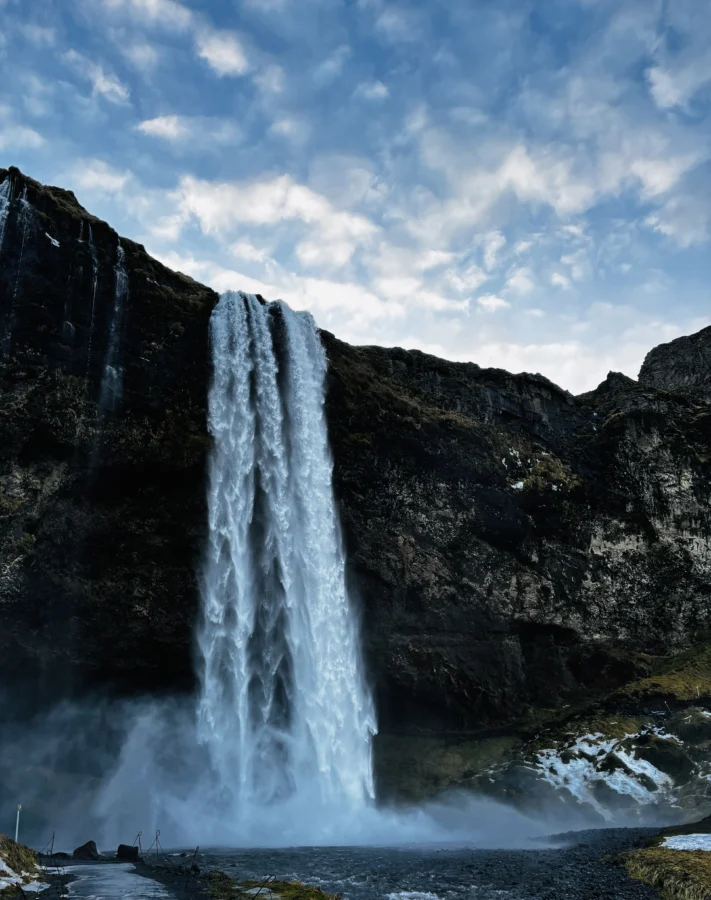 Seljalandsfoss in Iceland against a backdrop of half-cloudy sky.