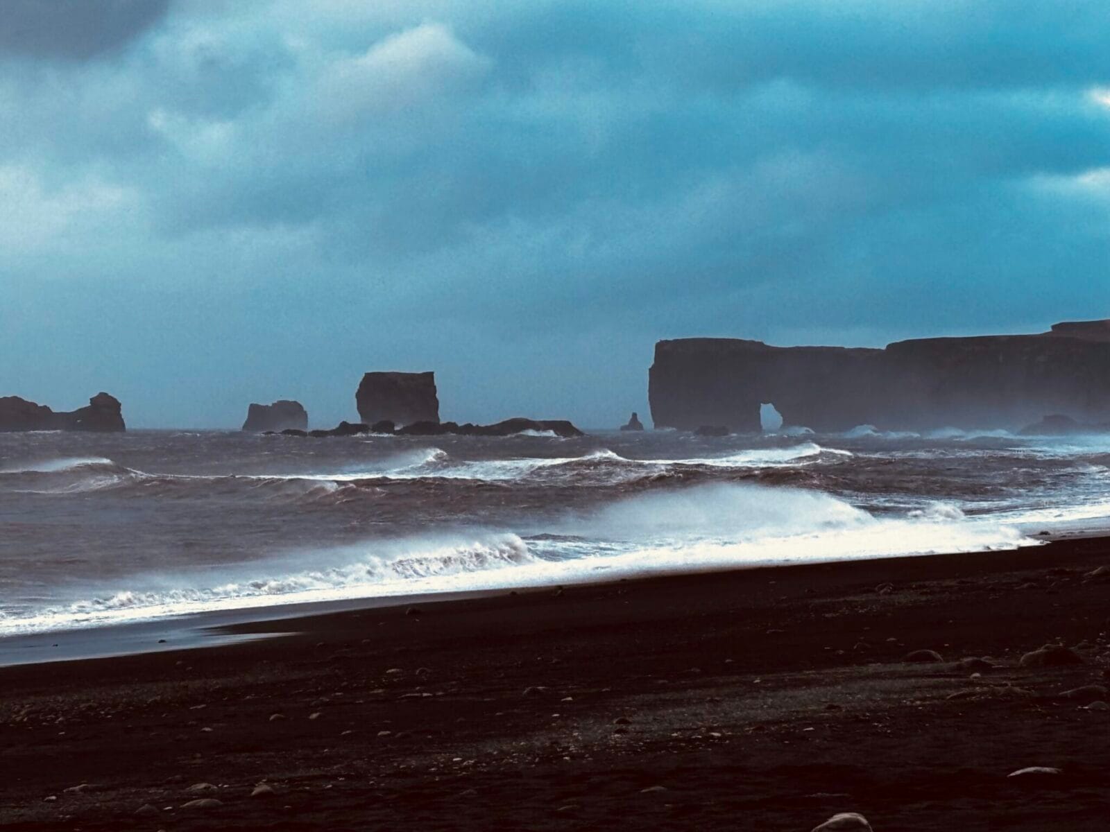 Reynisfjara black sand beach, Iceland, with waves crashing in and basalt formations in the background.