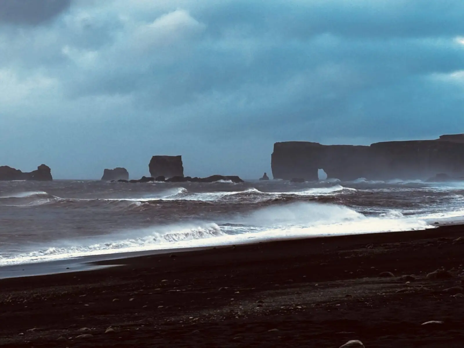 Reynisfjara black sand beach, Iceland, with waves crashing in and basalt formations in the background.