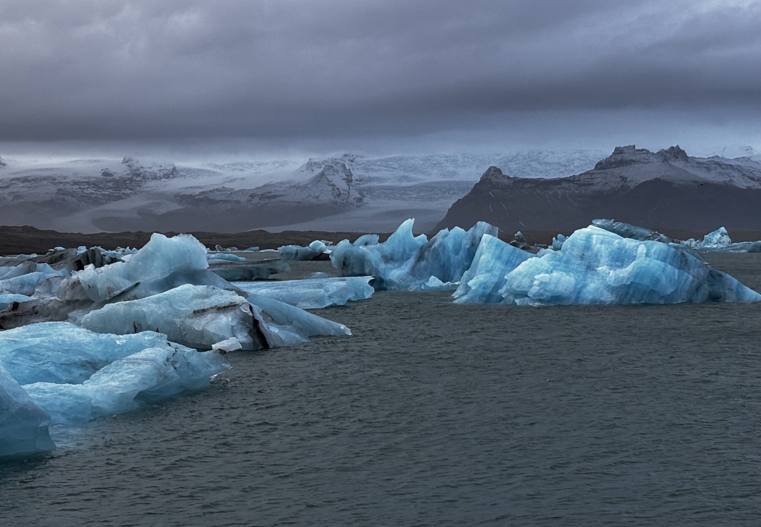 Jökulsárlón, Iceland: blue icebergs floating in the lagoon with a glacier and dark clouds in the background.