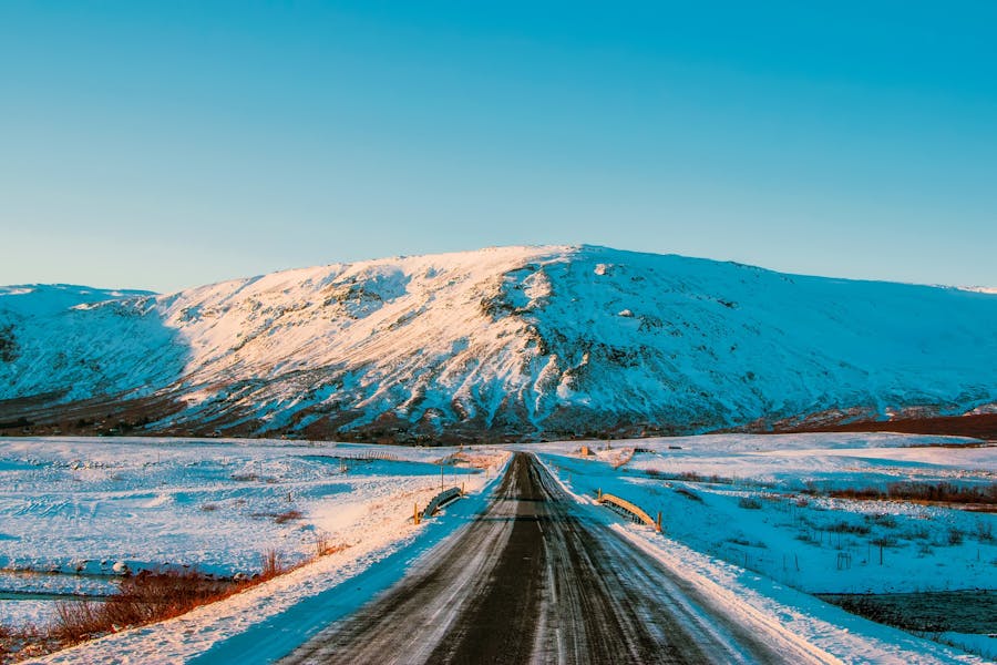 A picturesque winter road leading towards snow-capped mountains under a bright blue sky.