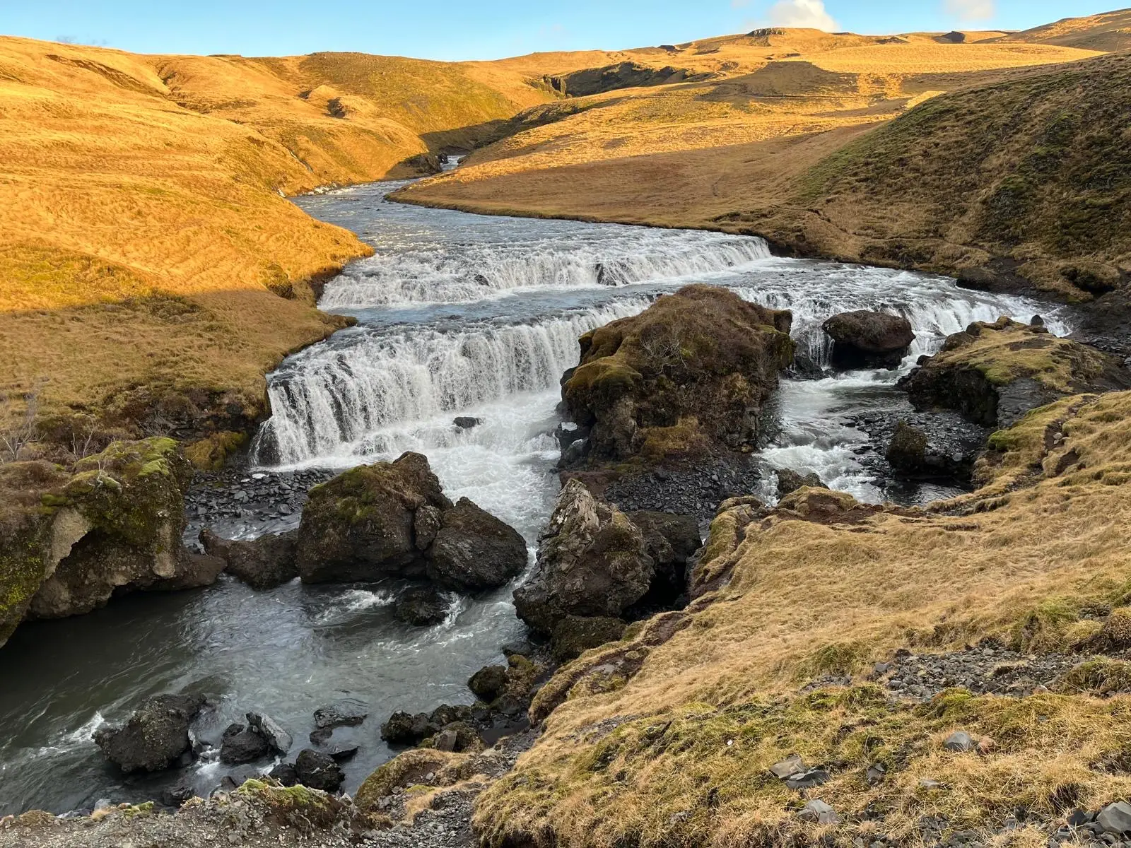 Skógafoss, Iceland, seen from above after climbing 500 steps up the stairs. Fast-flowing water surrounded by yellow grass and rocks