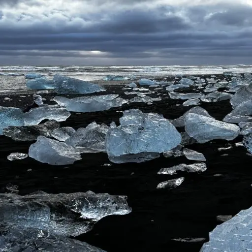 Large chunks of ice on a black sand beach, with sea and cloudy skies in the background. Diamond Beach, near Jökulsárlón, Iceland