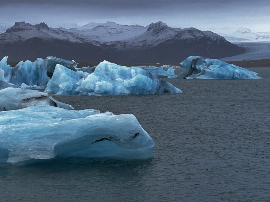 Blue icebergs floating on a glacier lagoon, with snow-capped mountains in the background