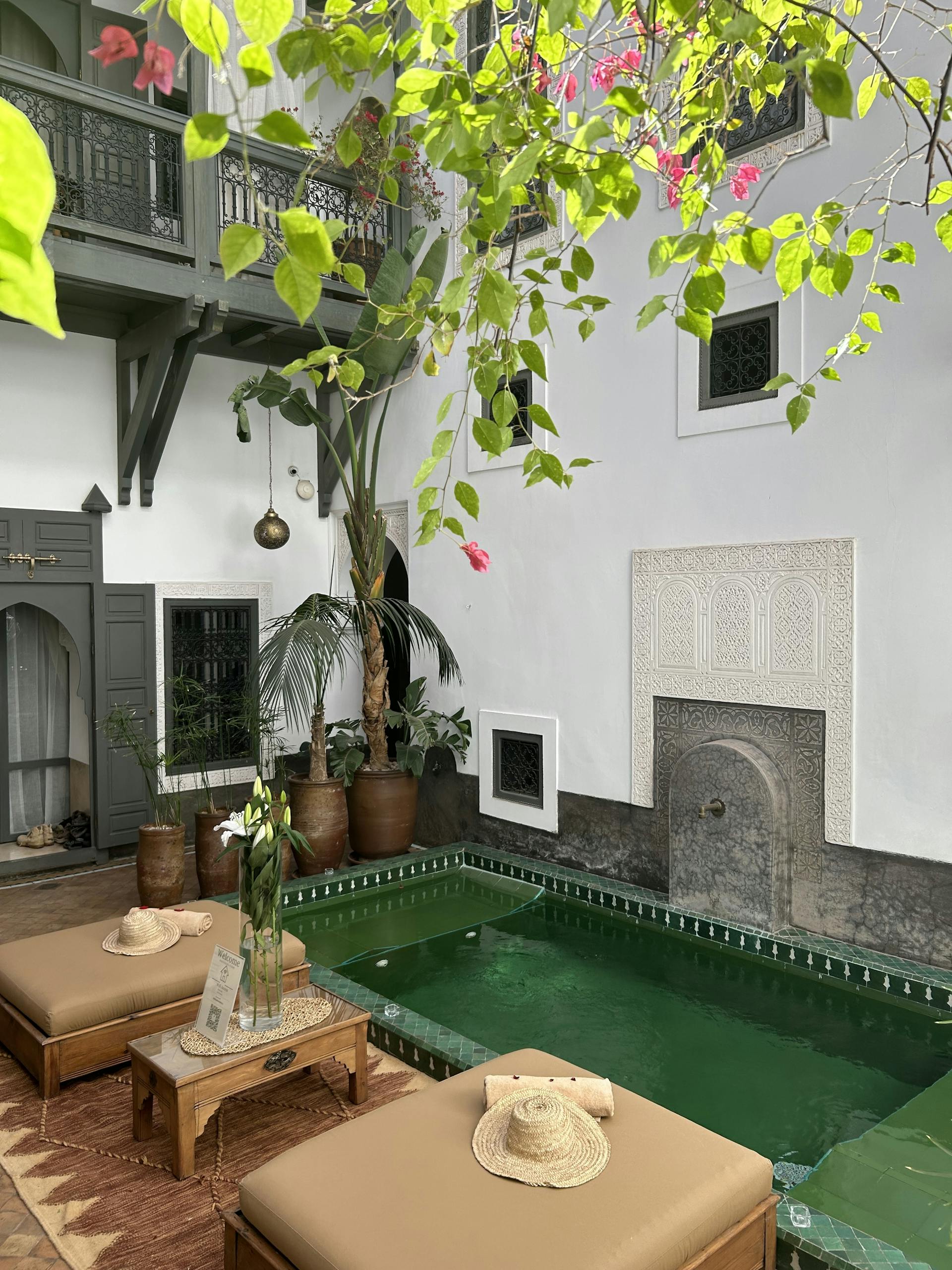 Charming Moroccan courtyard featuring a green pool, lush plants, and traditional architectural accents.