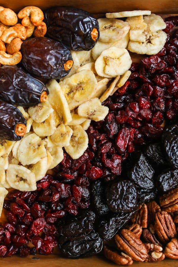 Colorful assortment of dried fruits and nuts, including bananas, dates, prunes, cranberries, pecans, and cashews.