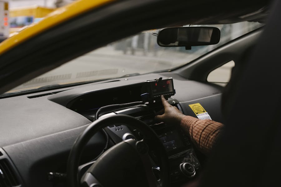 View inside a taxi with driver's hand on meter, capturing the steering wheel and dashboard.