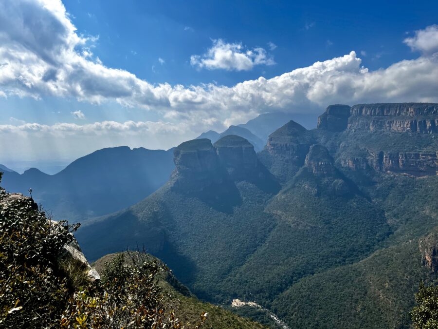 View over the Three Rondavels: green round mountain tops on a hazy day, with blue sky and some clouds