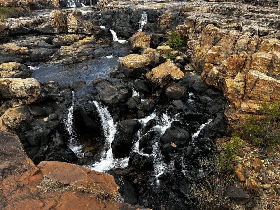 Waterfalls and rapids over red and black rocks, seen from above at Bourke's Luck Potholes