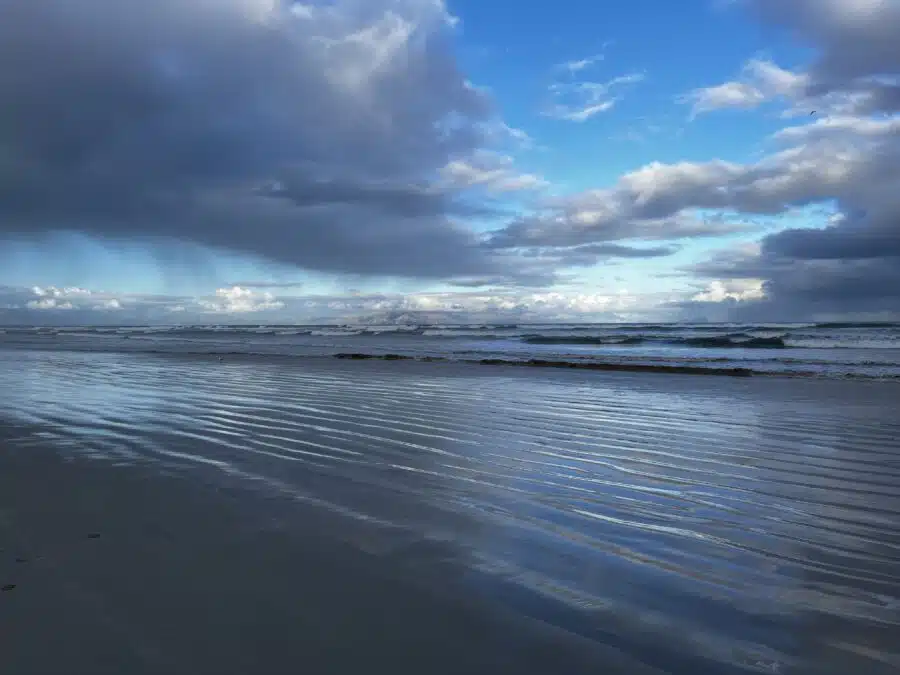 Beach Muizenberg with calm blue sea with small waves, blue sky, white clouds, near Cape Town 