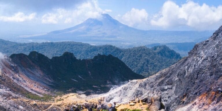 Large volcano in the distance, with rocky incline and crater rim in the foreground. Sumatra, Indonesia