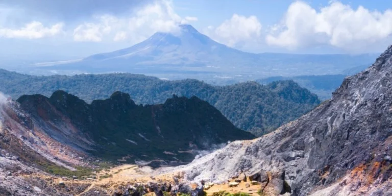 Large volcano in the distance, with rocky incline and crater rim in the foreground. Sumatra, Indonesia