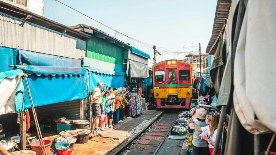 A bustling scene of a train navigating through the crowded railway market in Bangkok, Thailand.