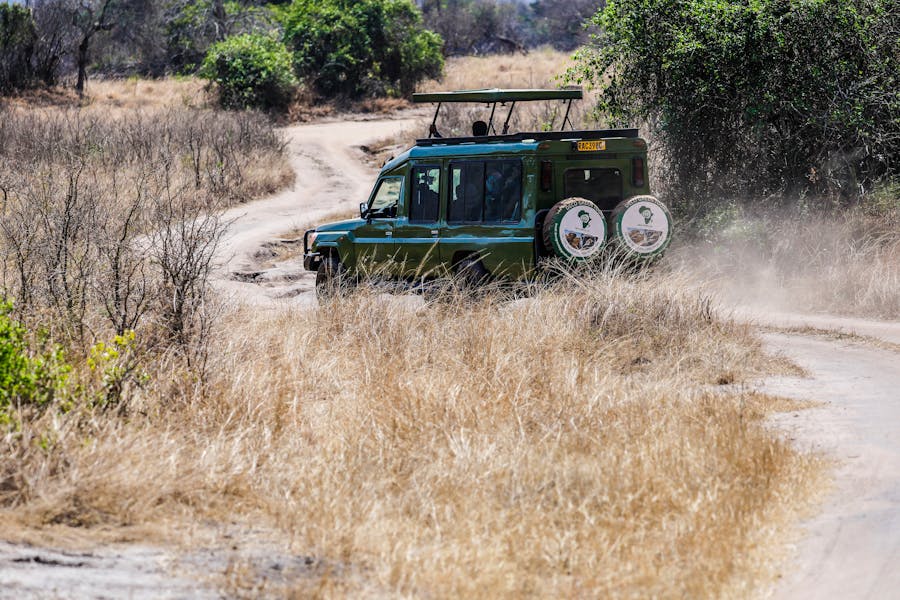 A green safari vehicle traverses a dusty trail through the African savanna.