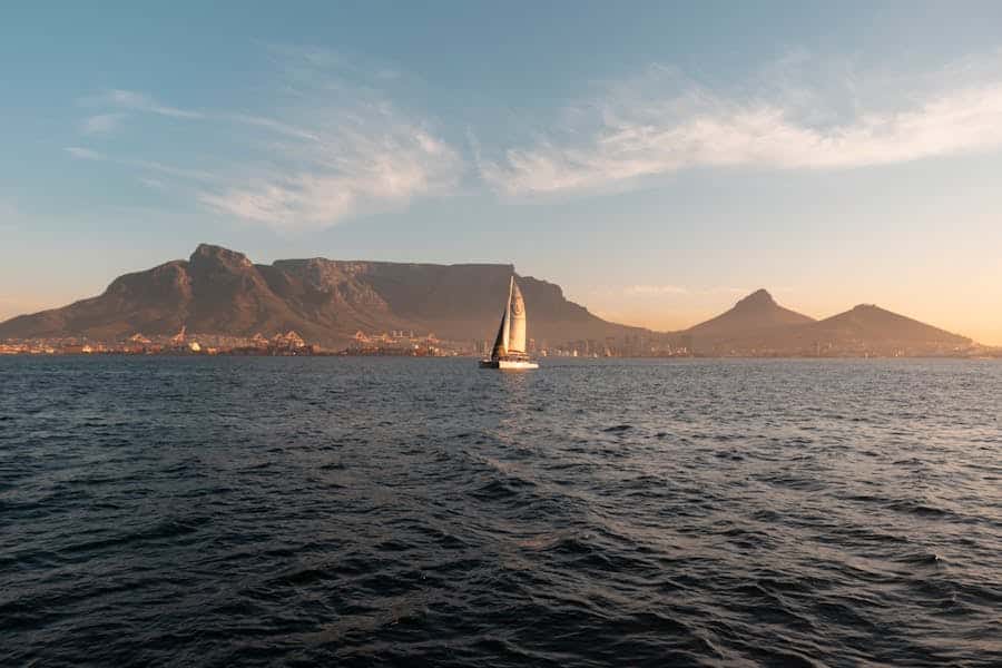 Sailboat navigating the ocean with Table Mountain and Cape Town in the backdrop during a serene sunset.