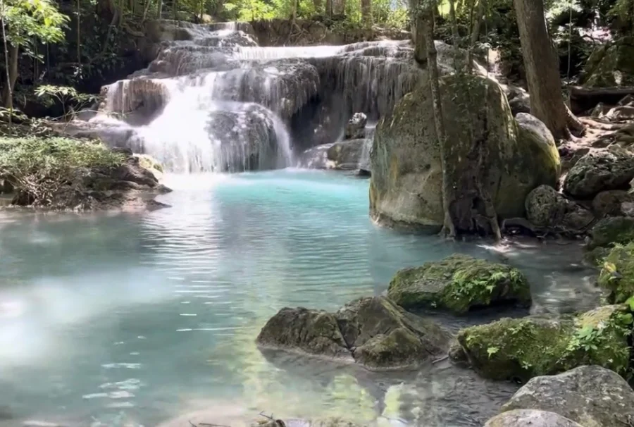 Level one at Erawan Falls in Kanchanaburi Province, Thailand. Water tumbling over rocks and falling into a turquoise pool. Surrounded by trees