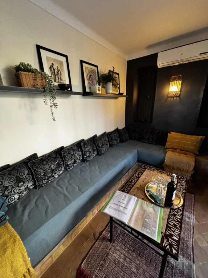 Photo: Tales From The Road Ahead. Interior of garden cottage in Villa Dinari, Marrakech. Blue sofa with throw pillows, table with tourist information.