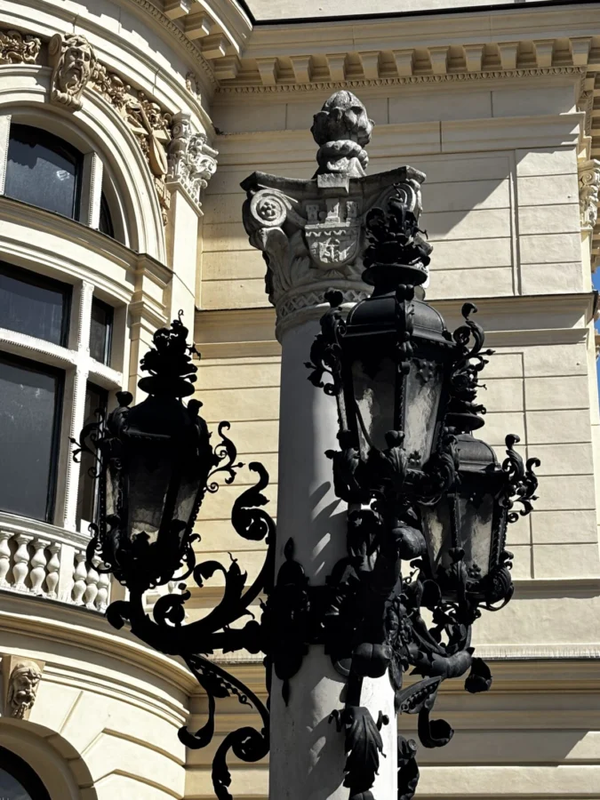 Photo: Tales From The Road Ahead. Lantern with intricate detail in cast iron. Seen against a beautifully decorated sand-coloured building on Rynek Główny, Kraków - the main square.