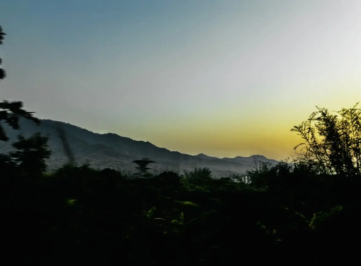 View of an early sunset with yellows and blues, over a mountain landscape, seen from a train in Thailand.
