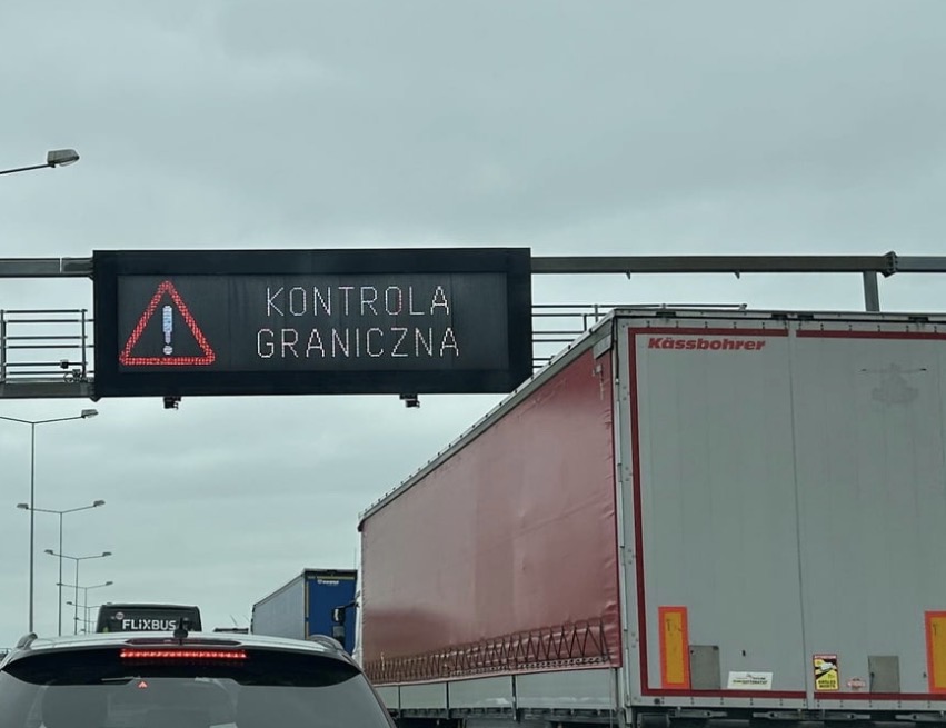 Sign above the road saying "Kontrola Graniczna", which is Polish for border checks. Large trucks and a Flixbus in the shot. 
