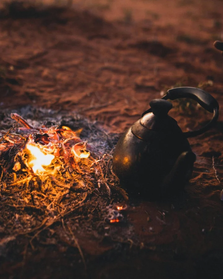 A serene campsite scene with a burning bonfire and a kettle on desert sand in Wadi Rum, Jordan.