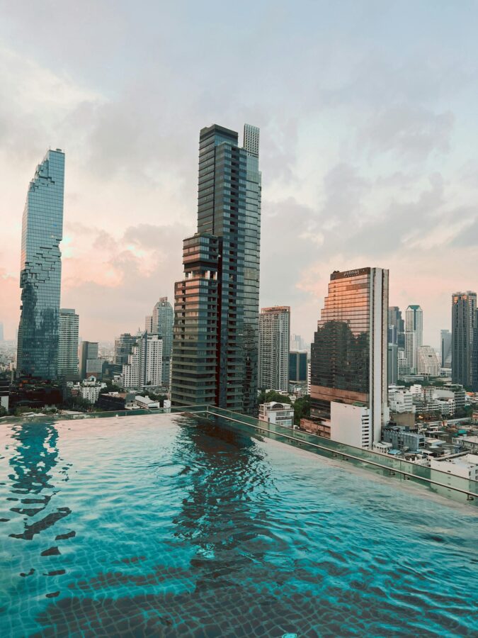 Breathtaking view of Bangkok skyline reflecting in a stylish rooftop pool at sunset.