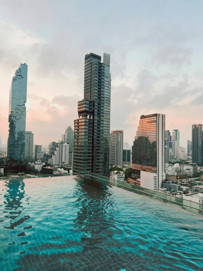 Breathtaking view of Bangkok skyline reflecting in a stylish rooftop pool at sunset.