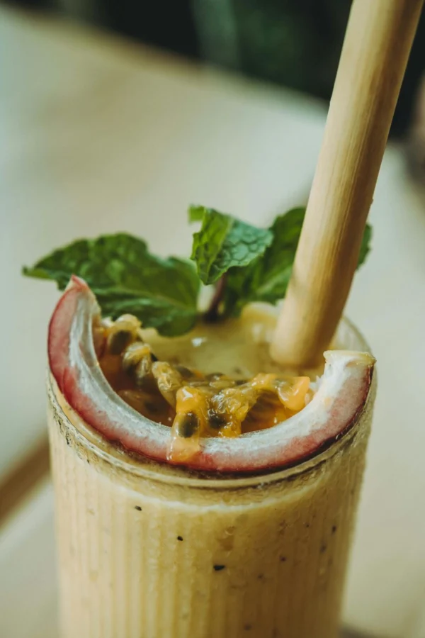 Close-up of a creamy passion fruit smoothie garnished with mint and served with a bamboo straw.