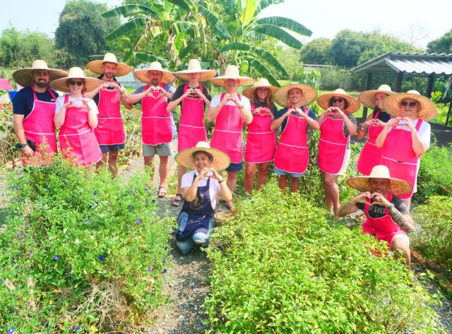 A group of people wearing pink aprons and traditional Thai hats, making heart shapes with their hands. 