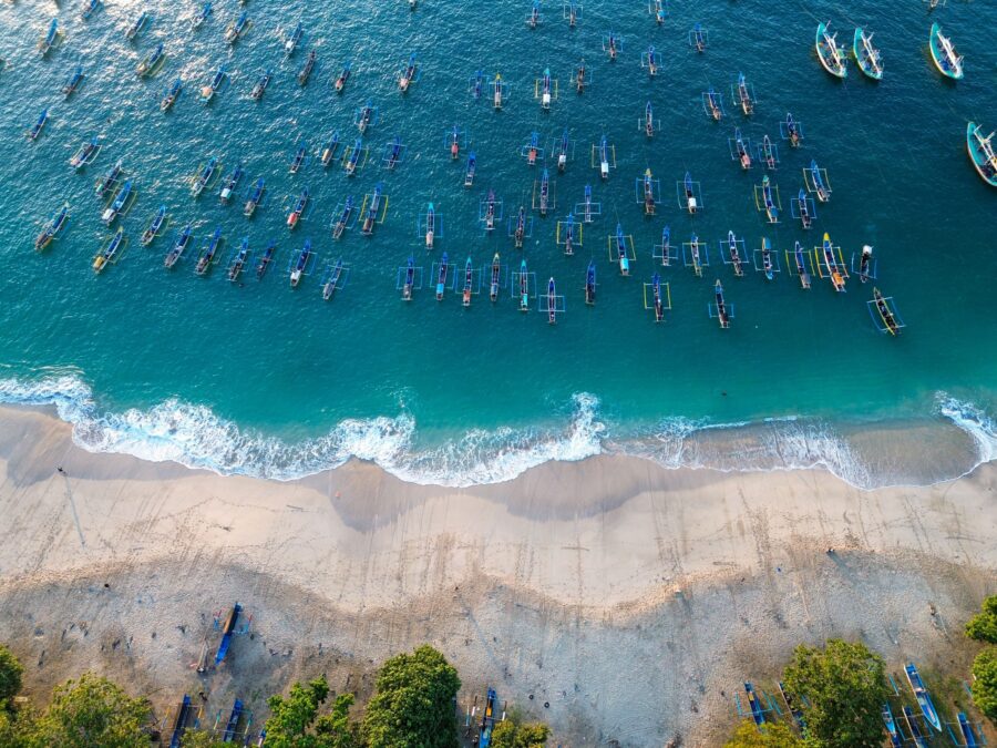 Aerial shot of colorful fishing boats in blue ocean near sandy beach and lush greenery.
