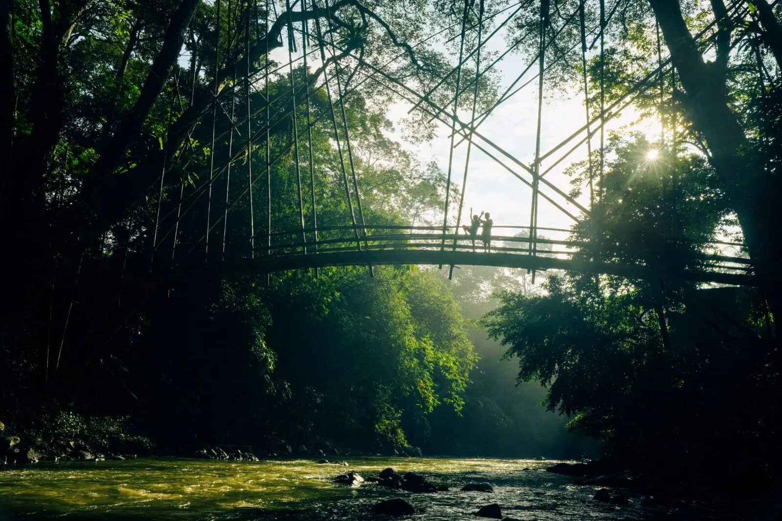 Silhouetted people on a bridge in Banten's lush jungle at sunrise, Indonesia.
