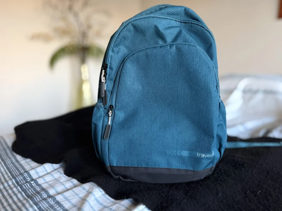 A bright teal backpack on a bed, with a blurred out plant in the background. Hand luggage for a trip to Indonesia